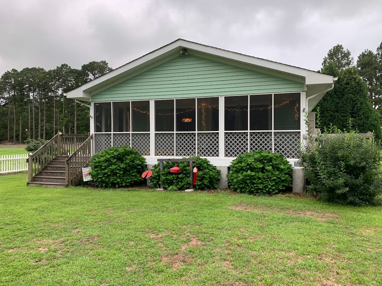 Green house with screen porch with bushes in the front.